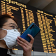 A passenger wearing a respiratory mask speaks on her smartphone by the departures board on January 31, 2020 at Rome’s Fiumicino airport